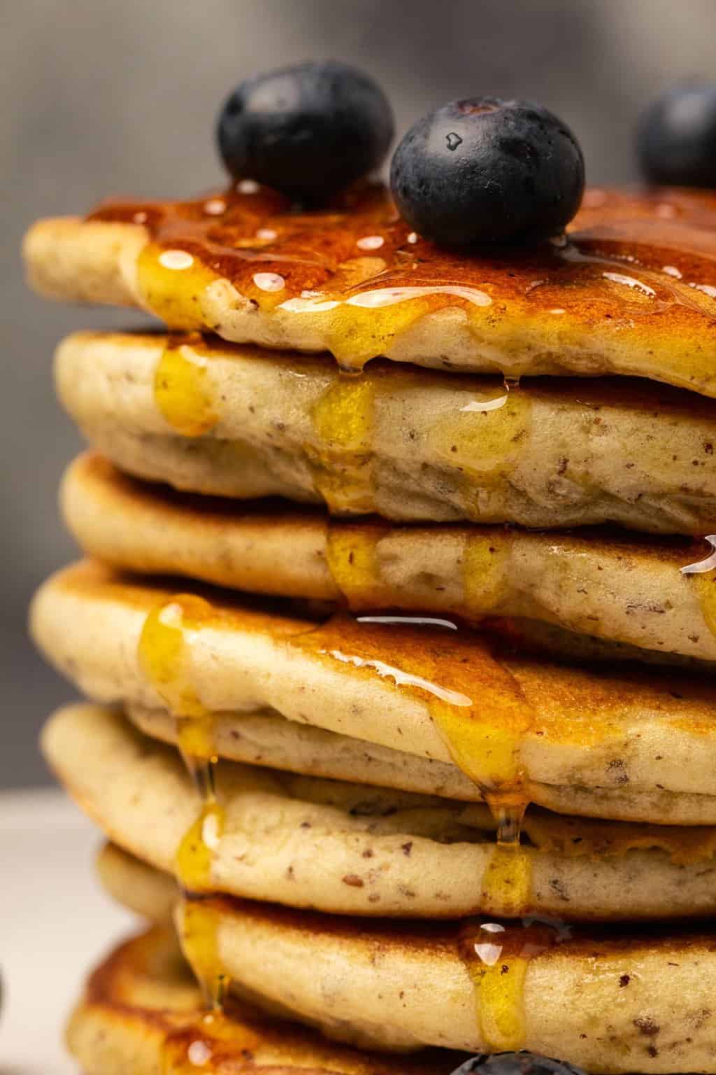 A stack of vegan gluten free pancakes drizzled with syrup and topped with fresh blueberries. 