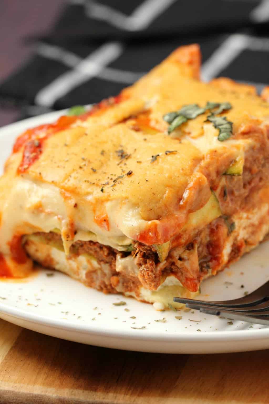 A slice of vegan lasagna on a white plate with a fork. 