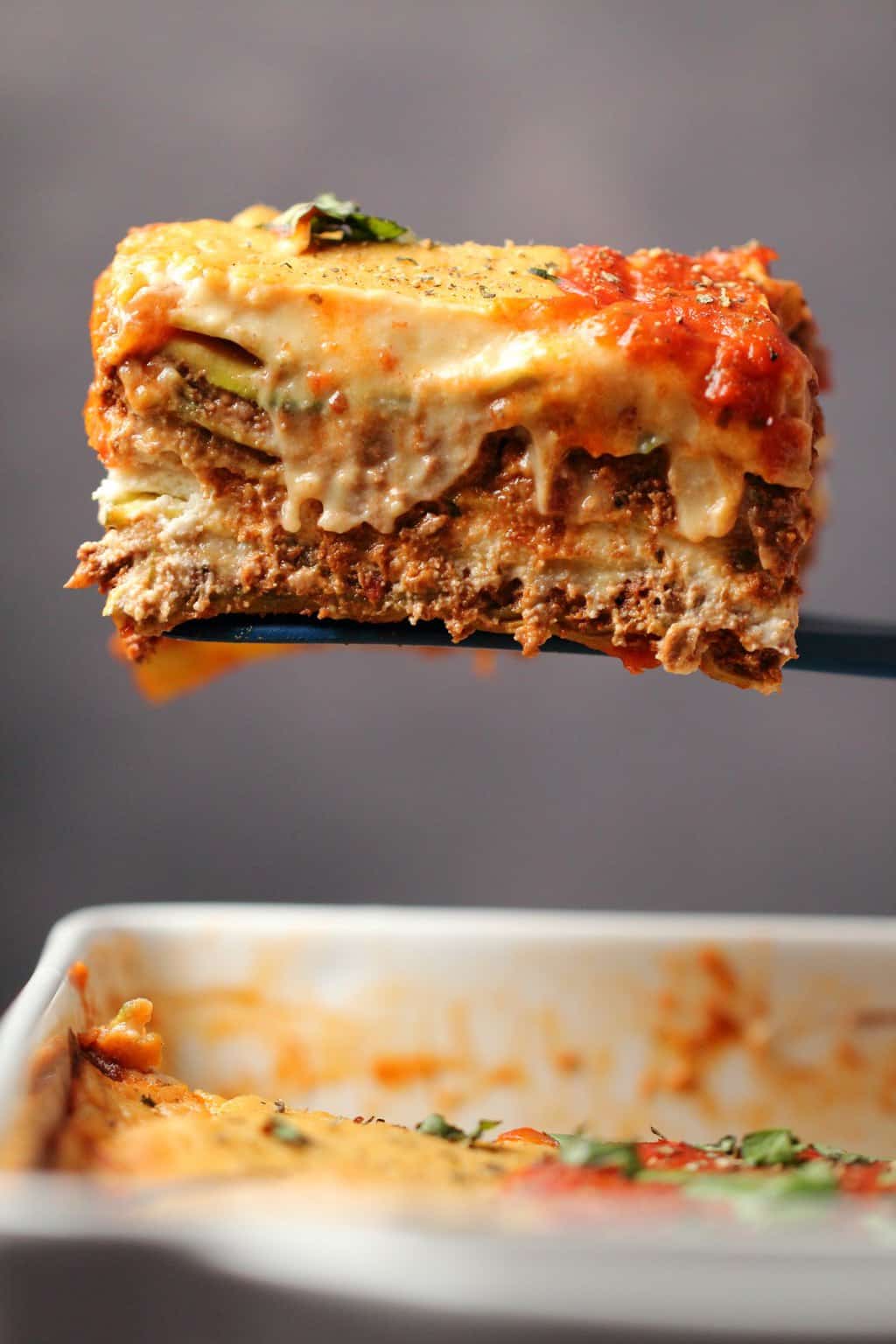 A slice of vegan lasagna lifting out of a white dish. 