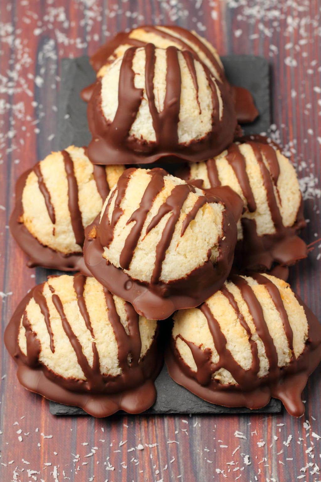 Vegan macaroons drizzled with chocolate stacked up on black tissue paper. 