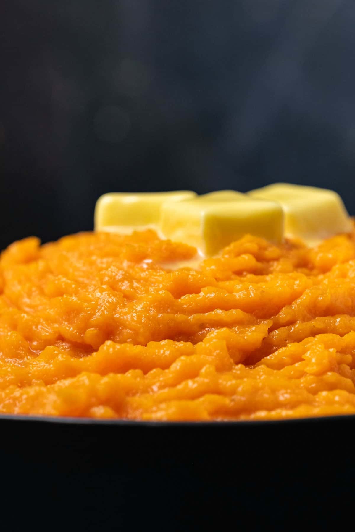 Vegan mashed sweet potatoes topped with butter in a black serving dish. 