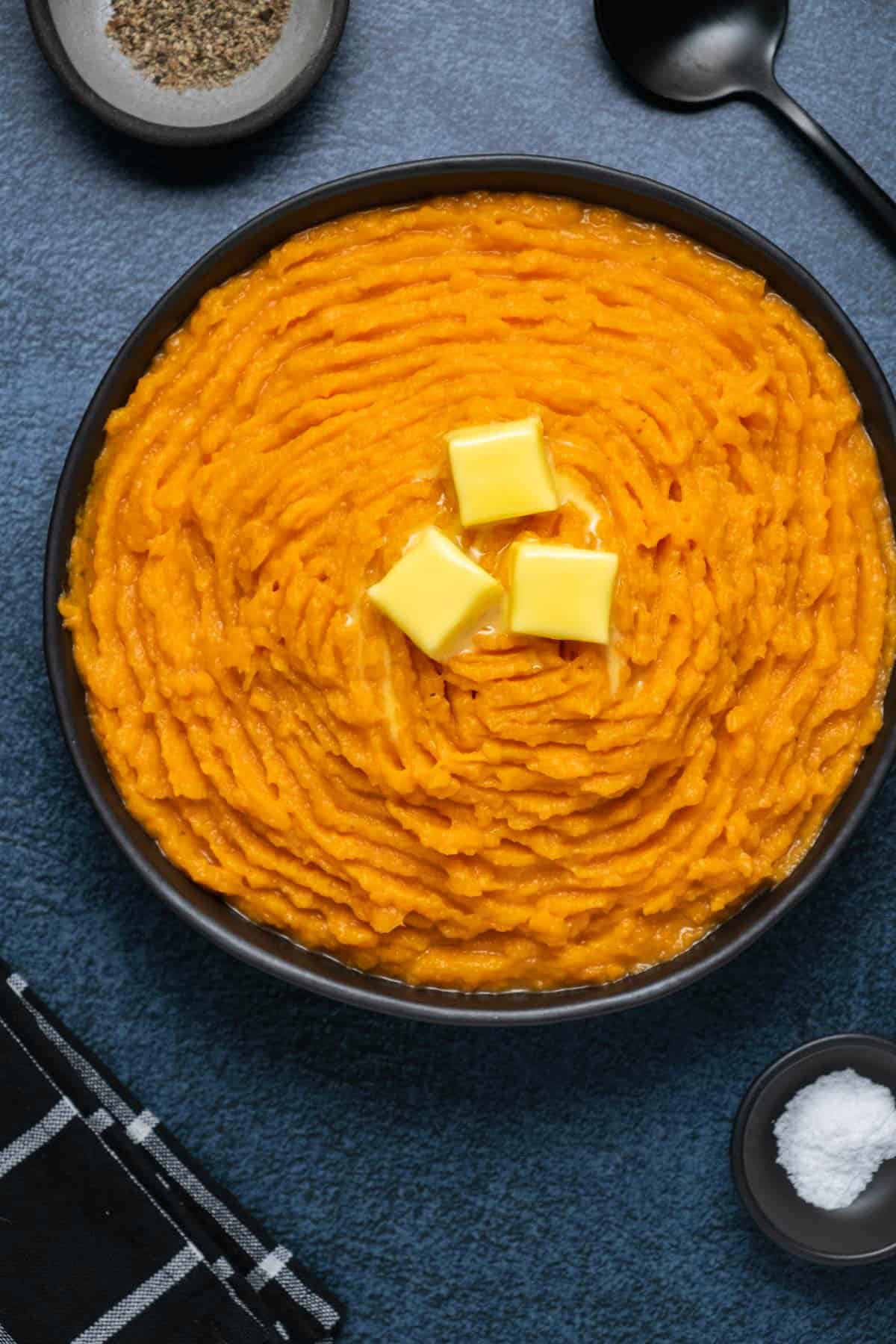 Vegan mashed sweet potatoes topped with vegan butter in a black bowl. 