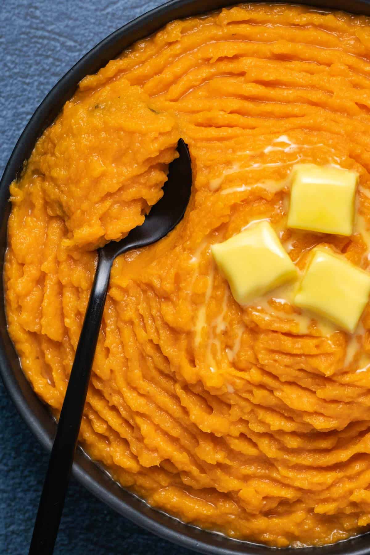 Vegan mashed sweet potatoes in a black bowl with a spoon. 