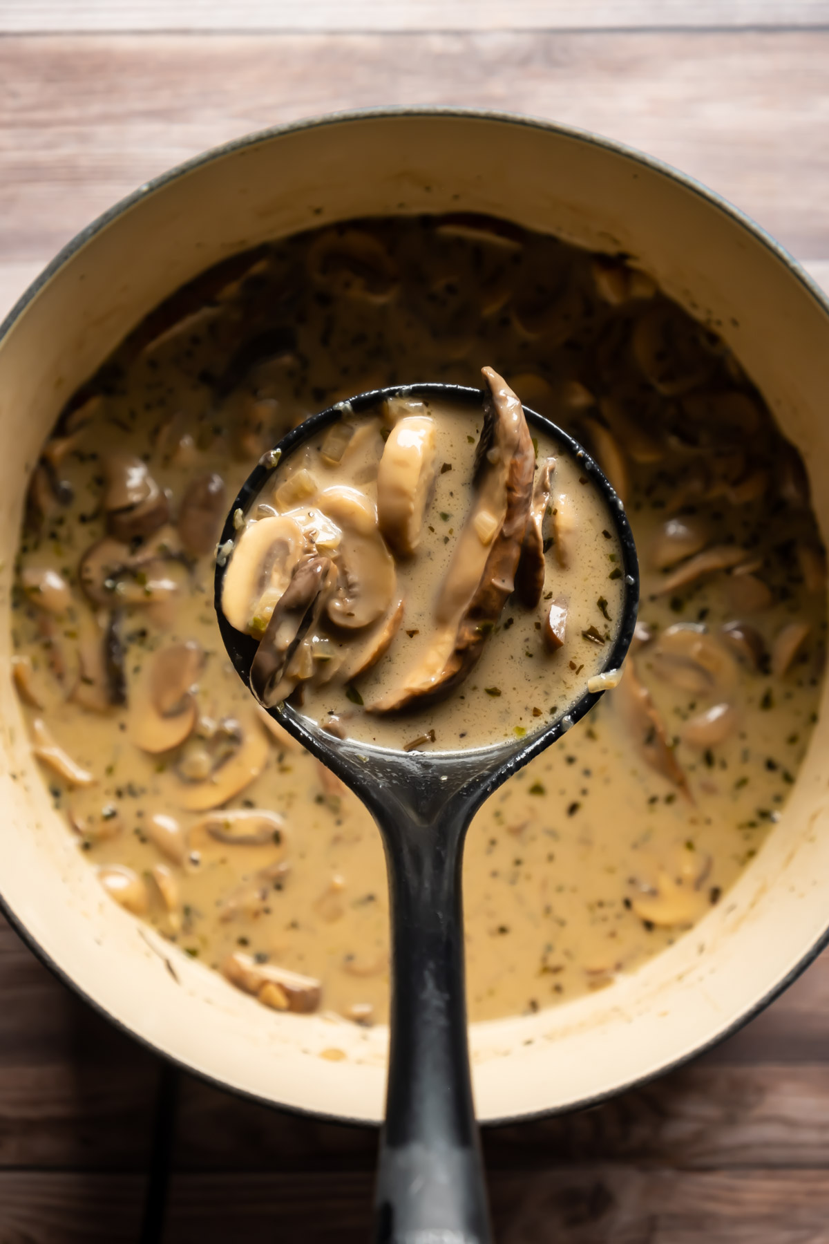 A soup ladle full of soup above a pot of vegan mushroom soup.