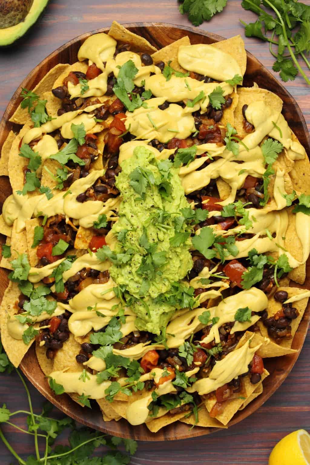 Vegan nacho cheese poured over fully loaded nachos with black beans, salsa and guacamole. 
