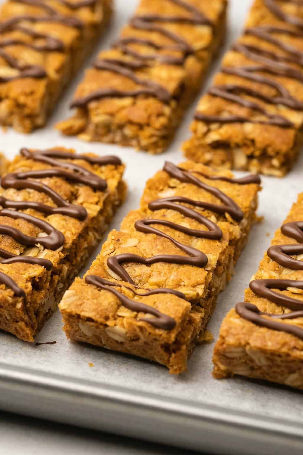Oatmeal bars drizzled with chocolate on a parchment lined baking tray. 