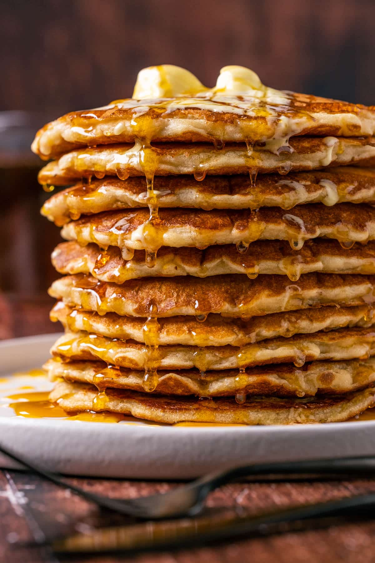 Stack of vegan oatmeal pancakes topped with vegan butter and syrup on a white plate. 