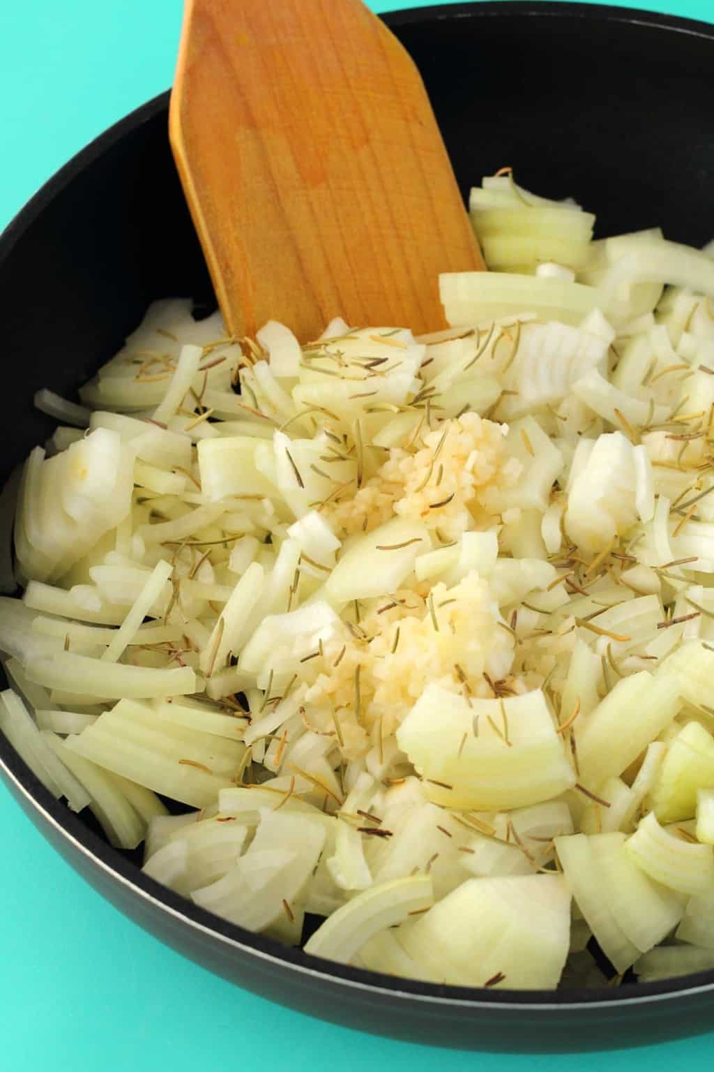 Sliced onions, rosemary and garlic in a frying pan with a wooden spoon. 