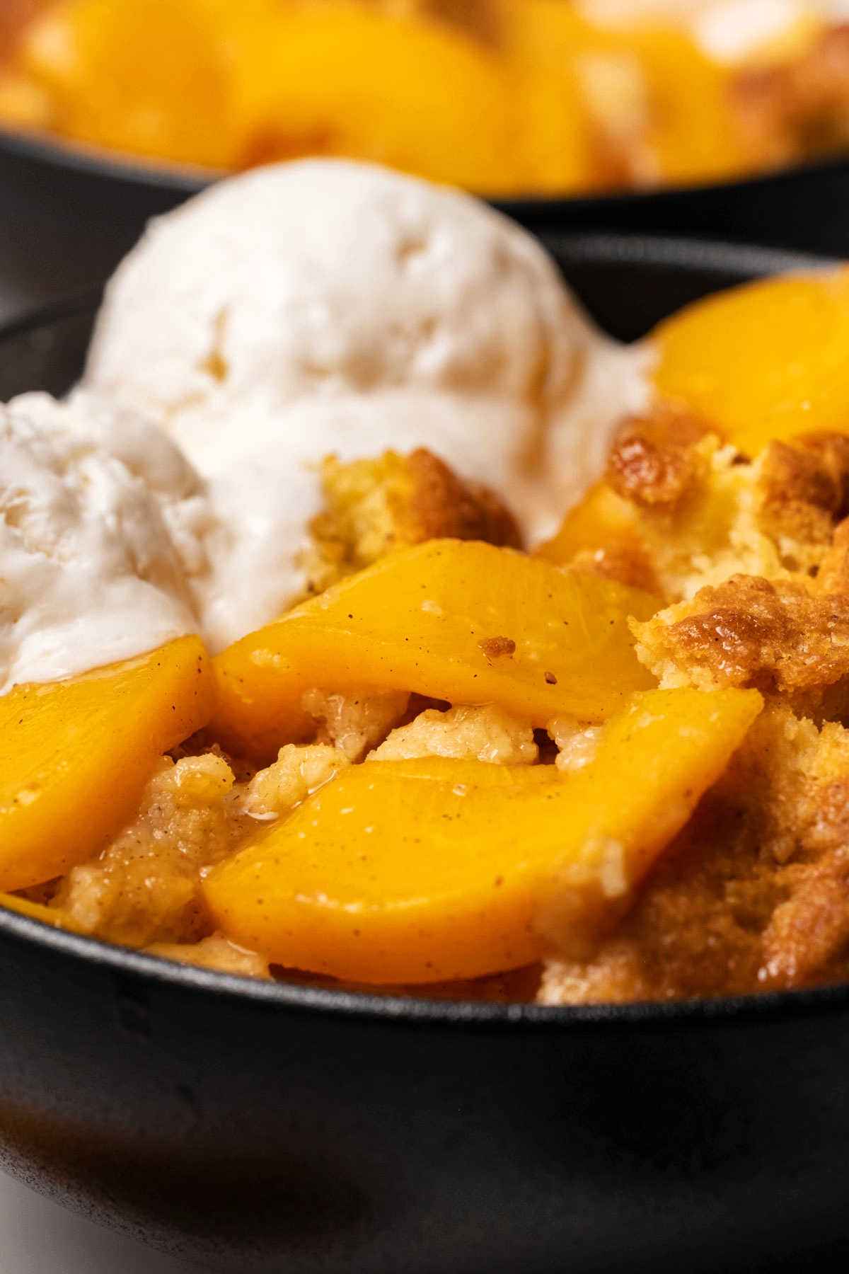 Close up photo of vegan peach cobbler in a black bowl with ice cream. 