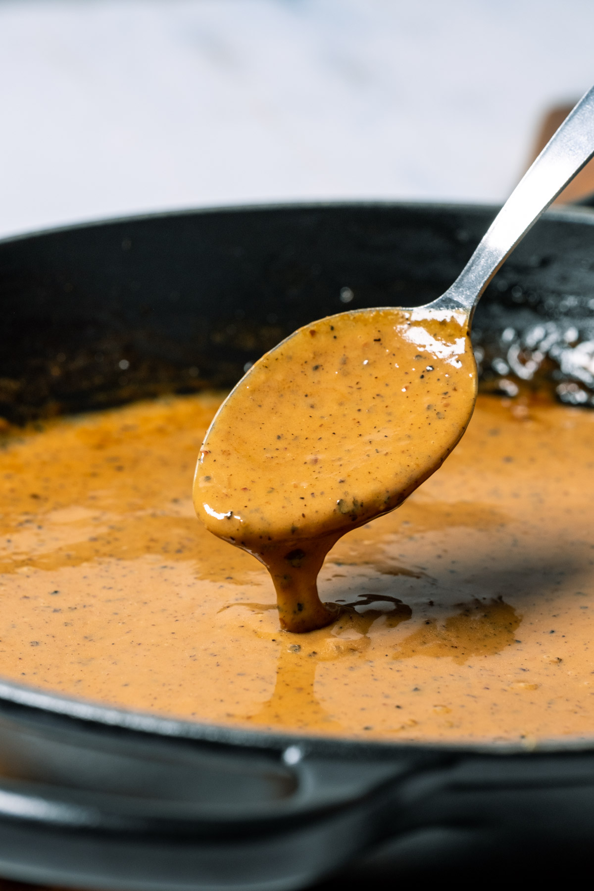 Vegan peppercorn sauce in a black skillet with a spoon.