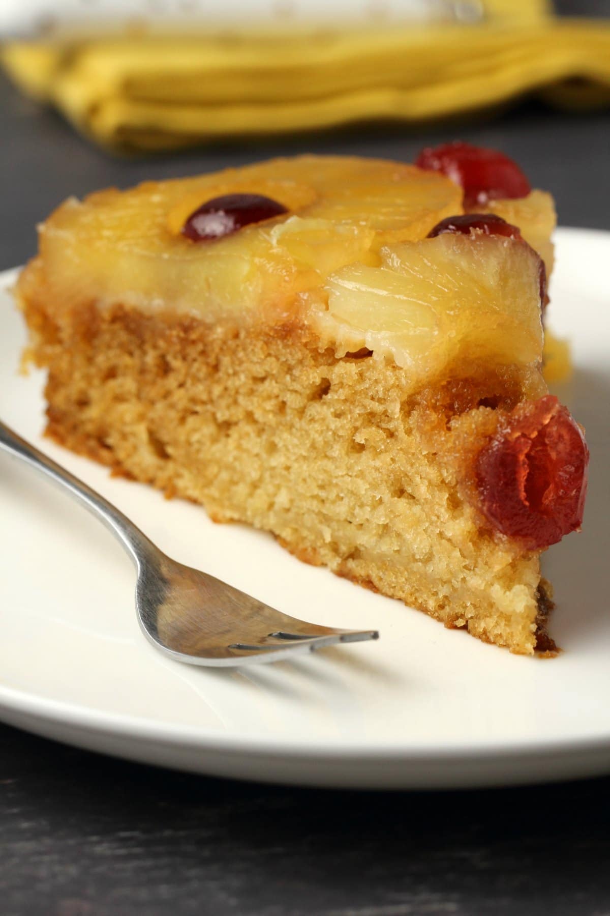 A slice of vegan pineapple upside down cake on a white plate with a cake fork.