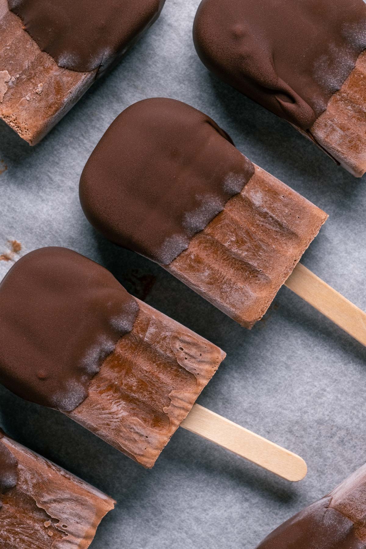 Chocolate dipped popsicles on a parchment lined tray.