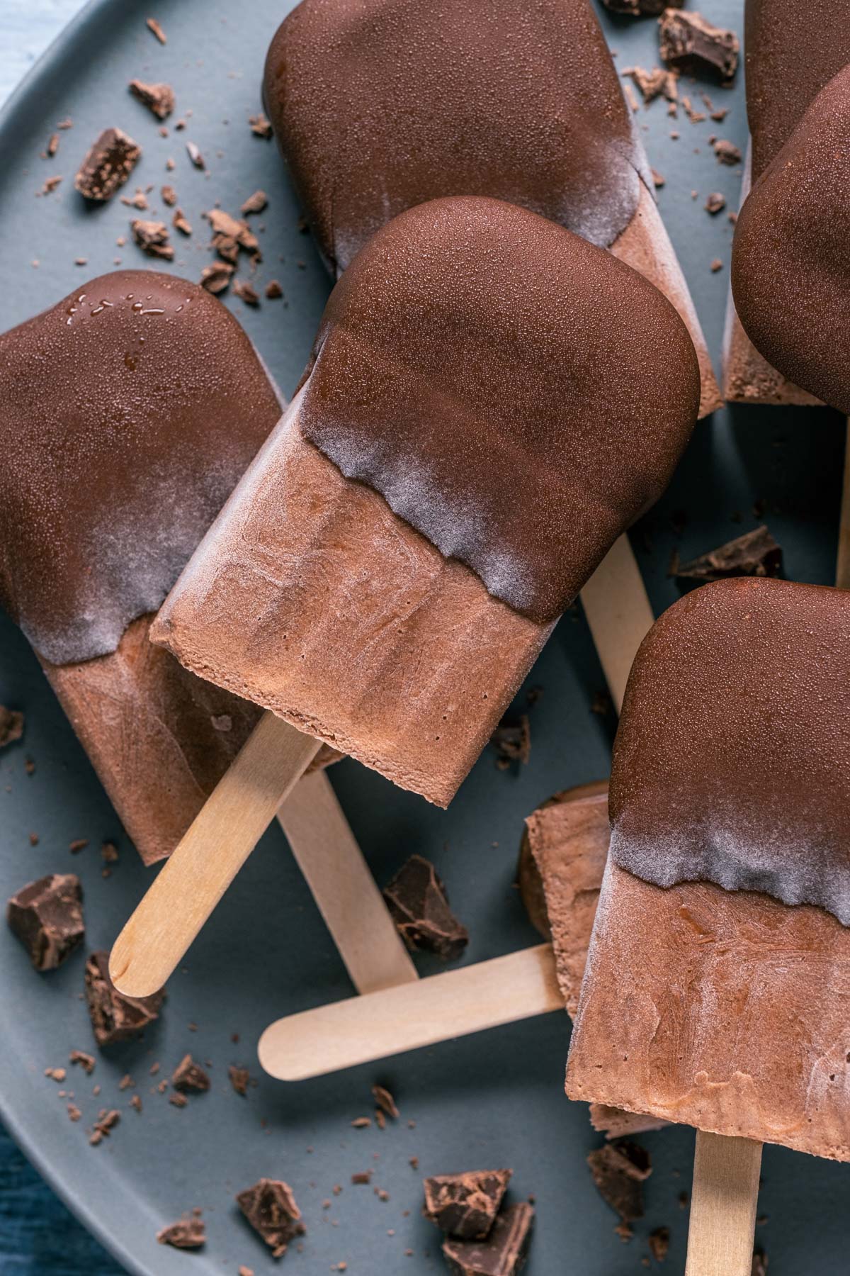 Chocolate dipped popsicles stacked up on a plate. 