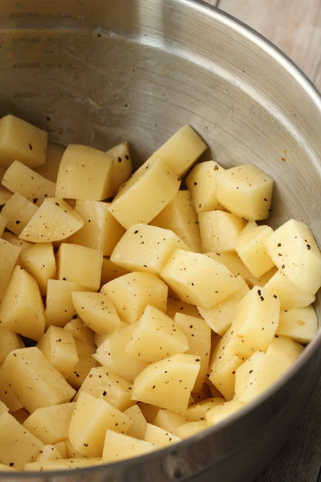 Peeled and chopped potato in a bowl with olive oil and salt and pepper. 