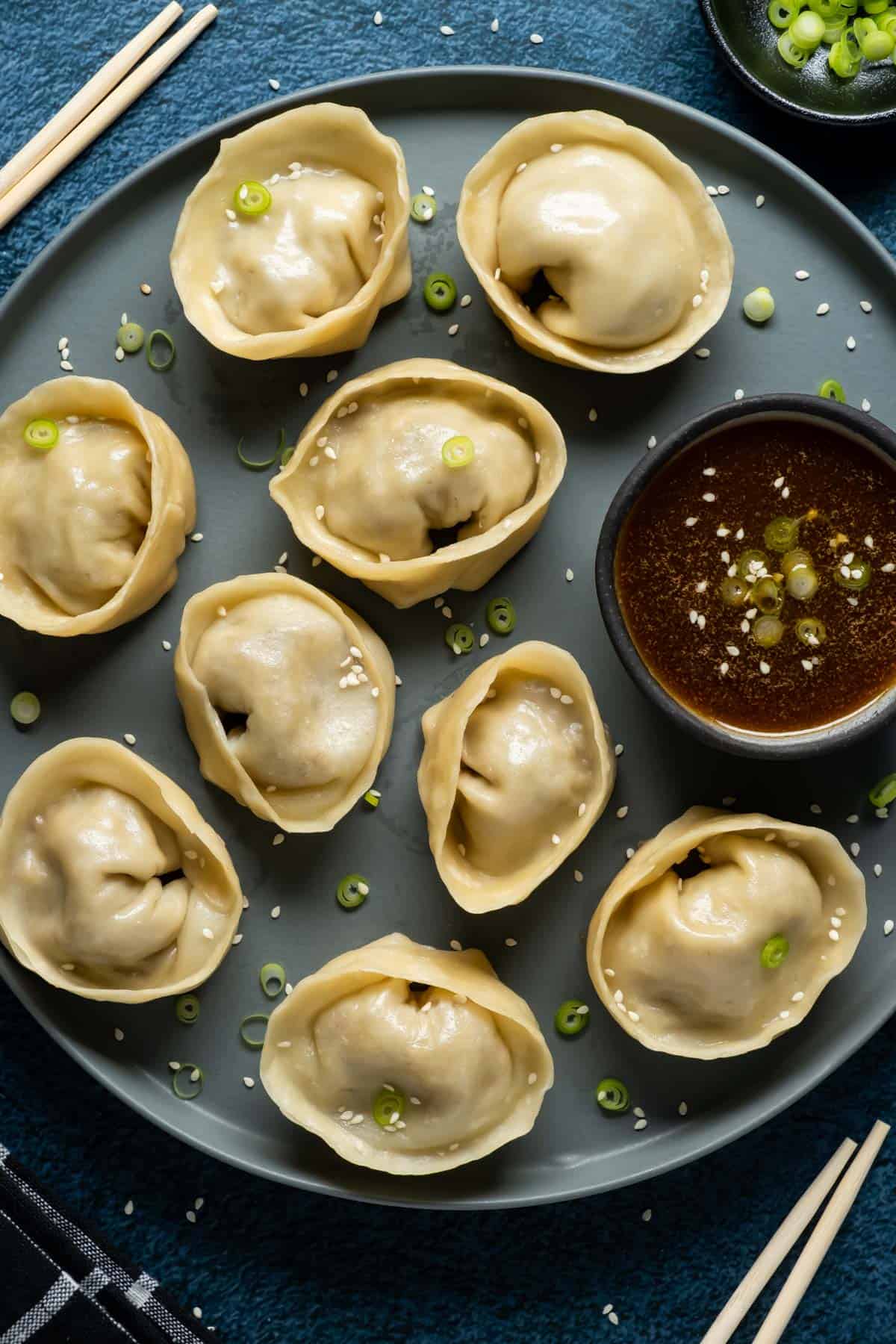 Dumplings topped with chopped green onions on a plate with dipping sauce.