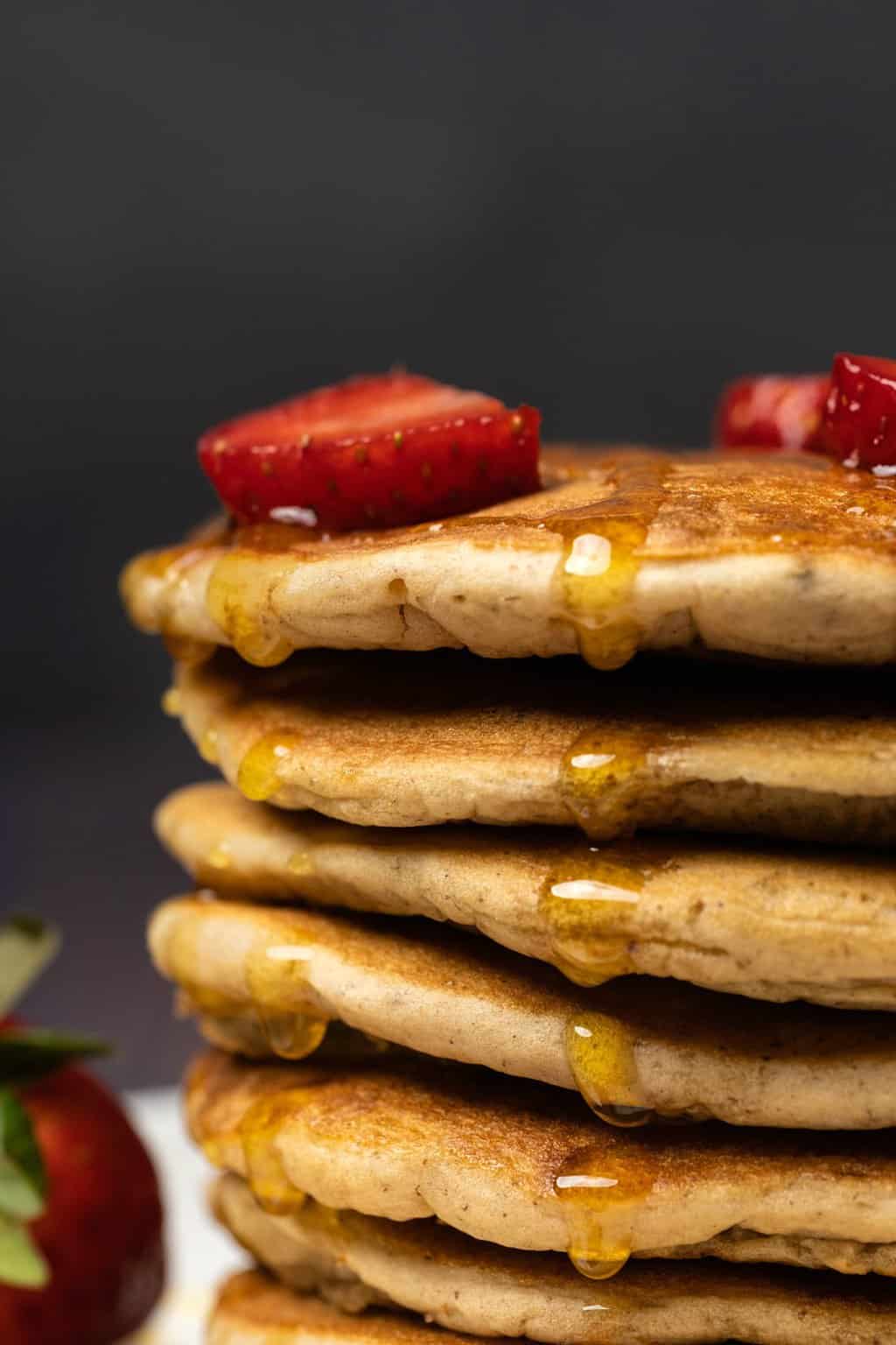 A stack of pancakes topped with strawberries and drizzled with syrup. 
