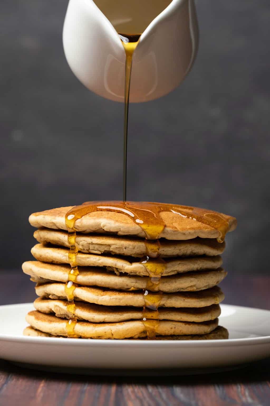 A stack of vegan protein pancakes with syrup pouring over the top. 
