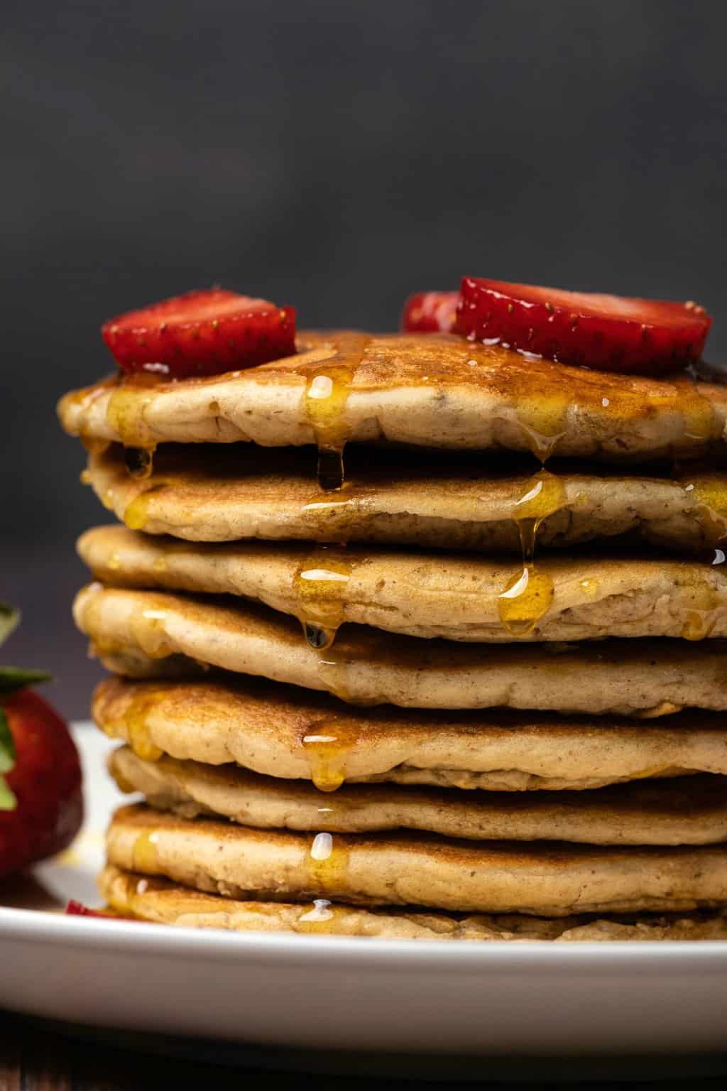 Vegan protein pancakes drizzled with syrup and topped with strawberries. 