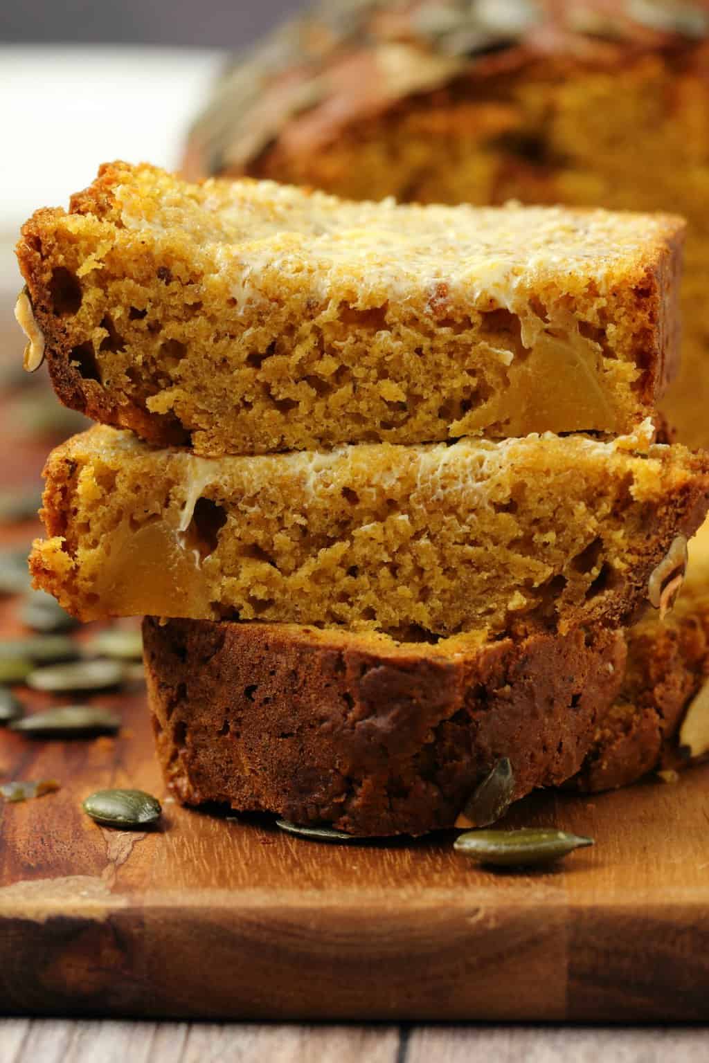 Slices of vegan pumpkin bread stacked up on a wooden board. 