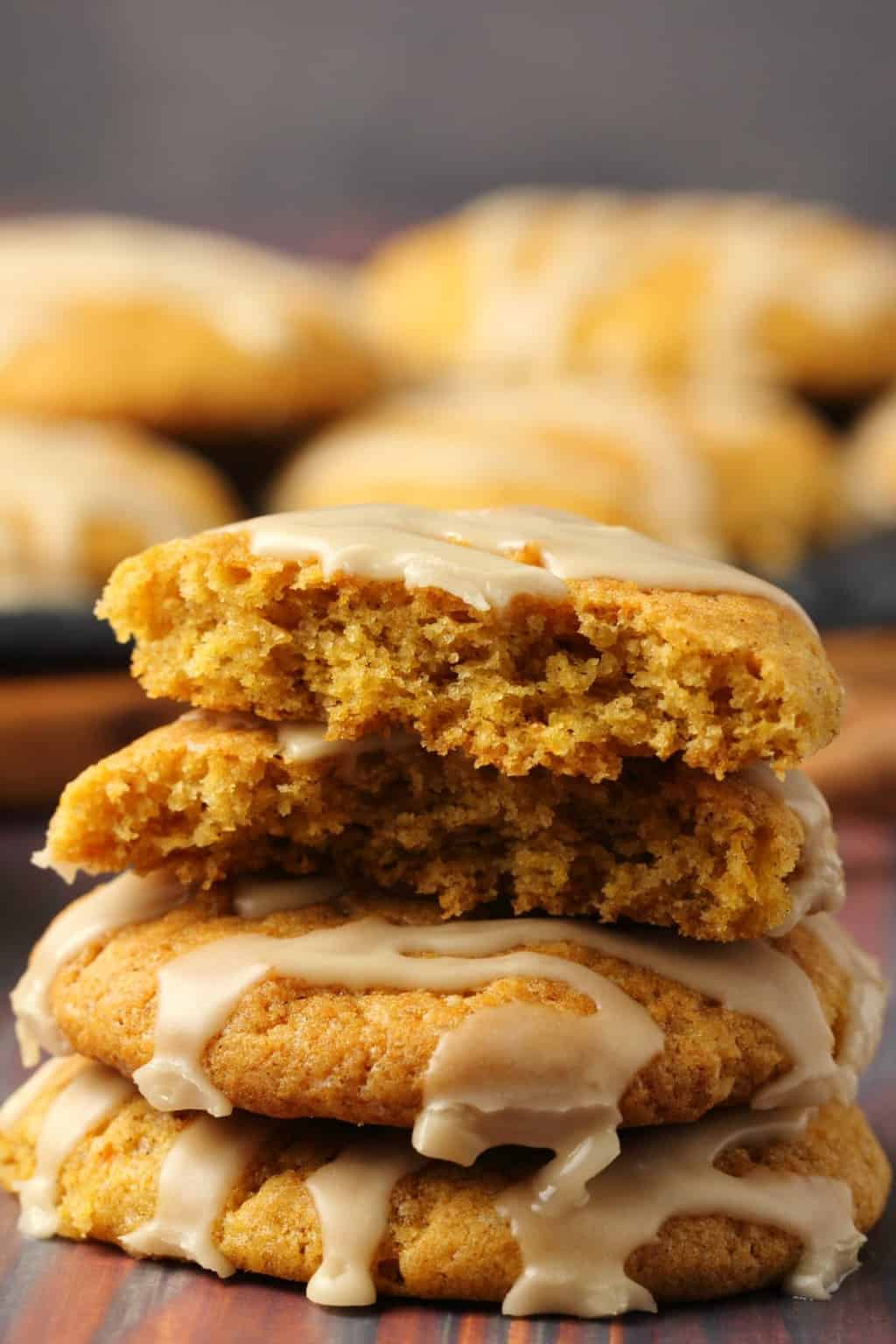 A stack of vegan pumpkin cookies topped with maple glaze, the top cookie broken in half to show the center. 