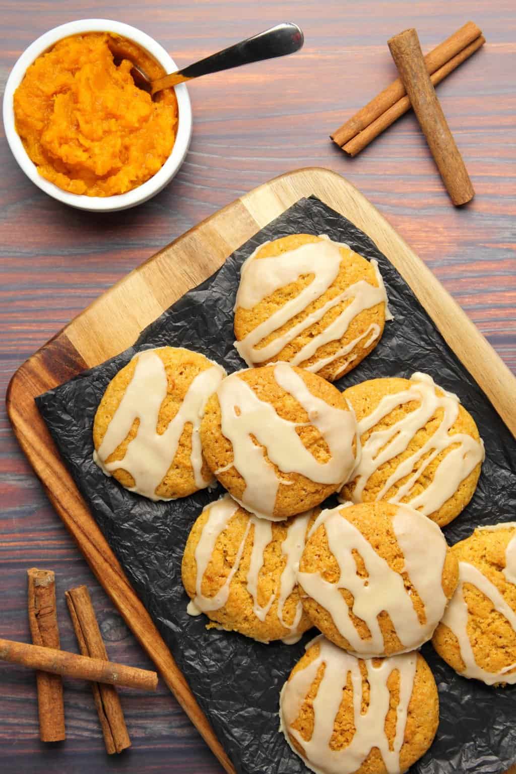 Vegan pumpkin cookies topped with a maple glaze stacked on a wooden board. 