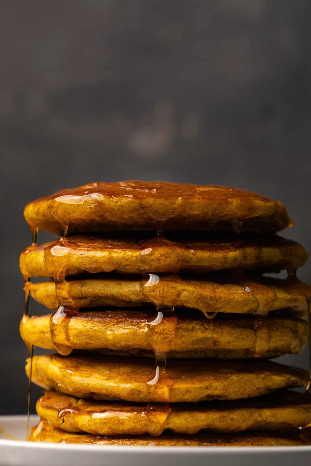 A stack of vegan pumpkin pancakes drizzled with syrup on a white plate. 