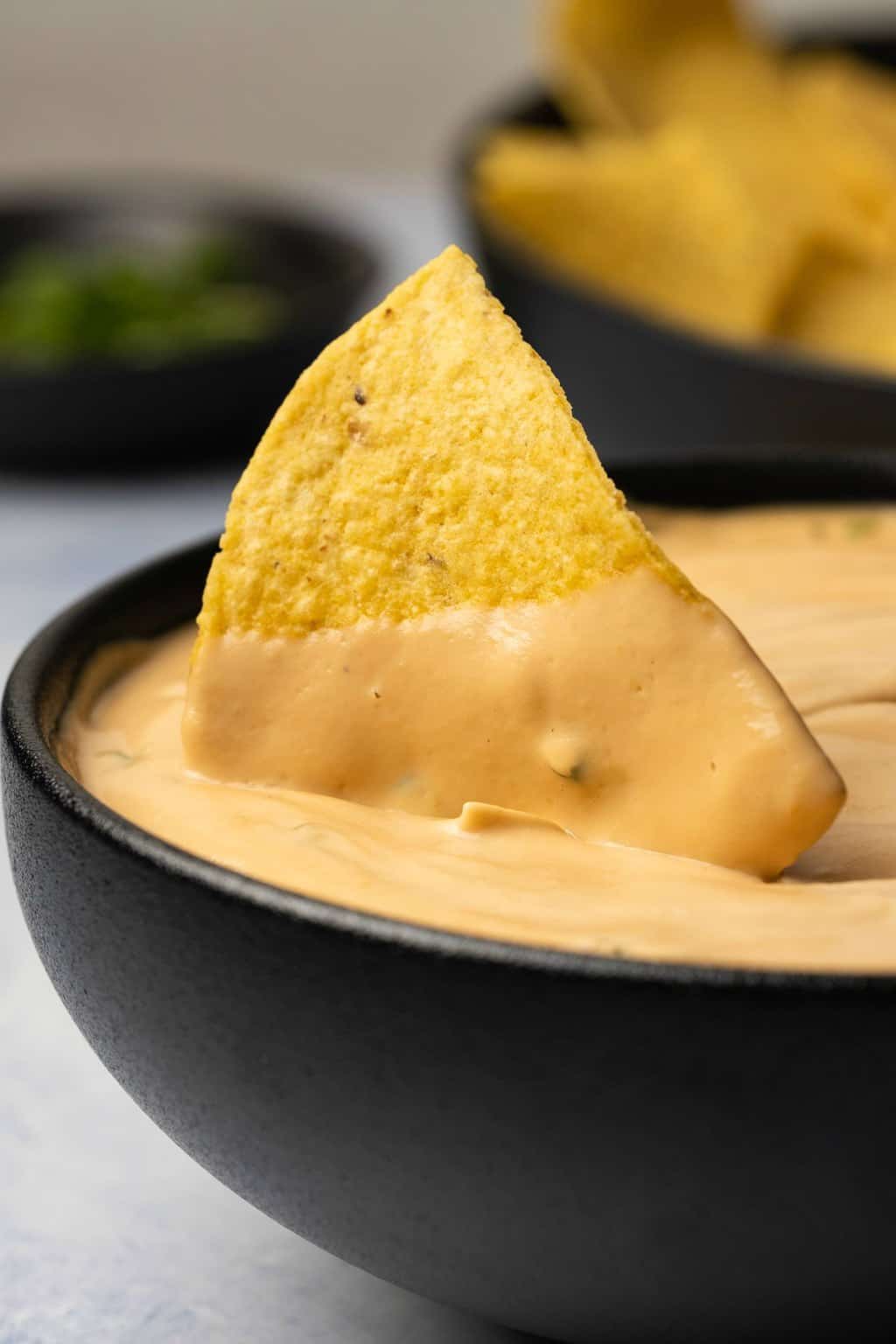 Tortilla chip in a black bowl of queso. 