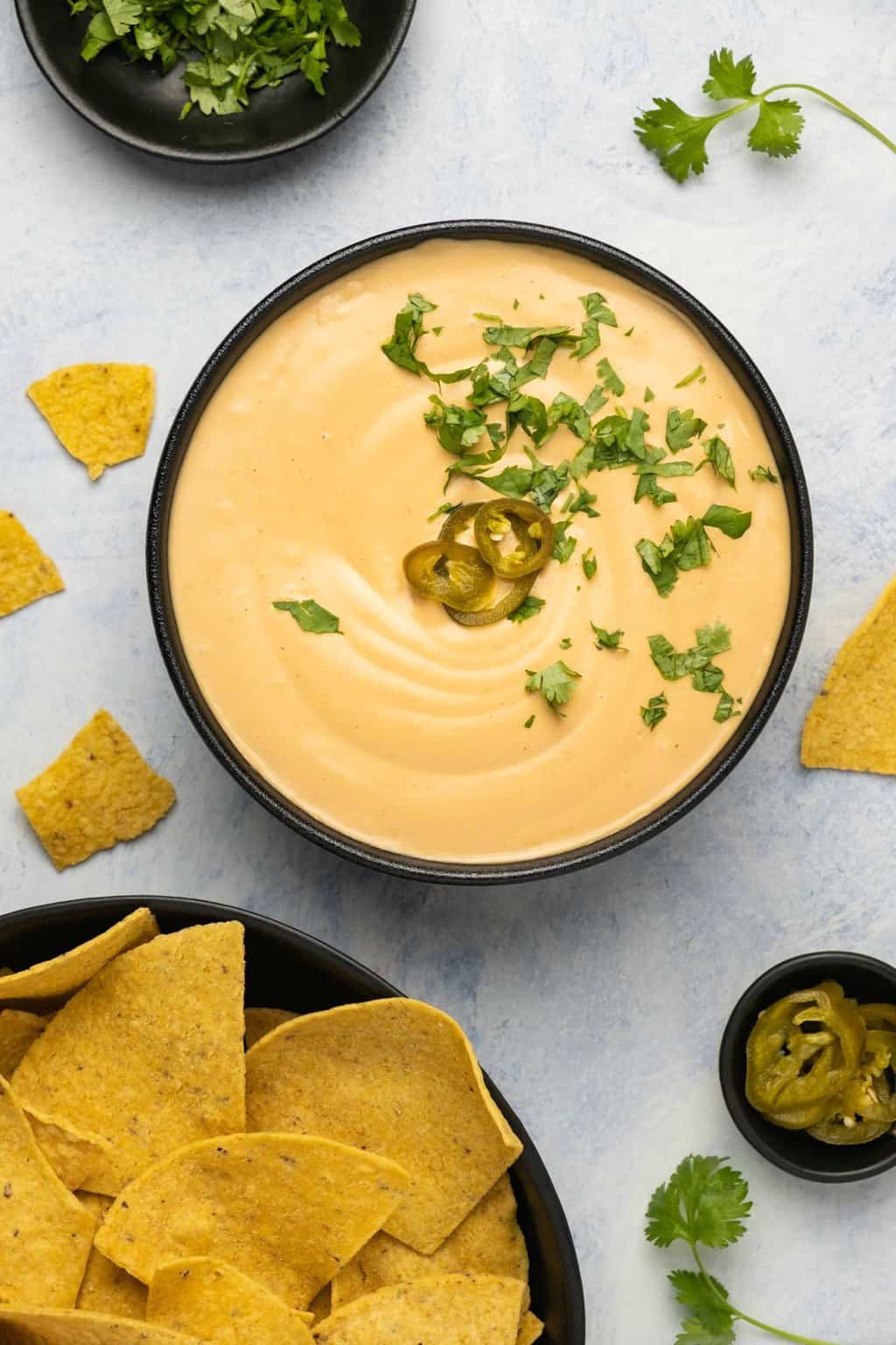 Vegan queso topped with sliced jalapeños and chopped cilantro in a black bowl. 