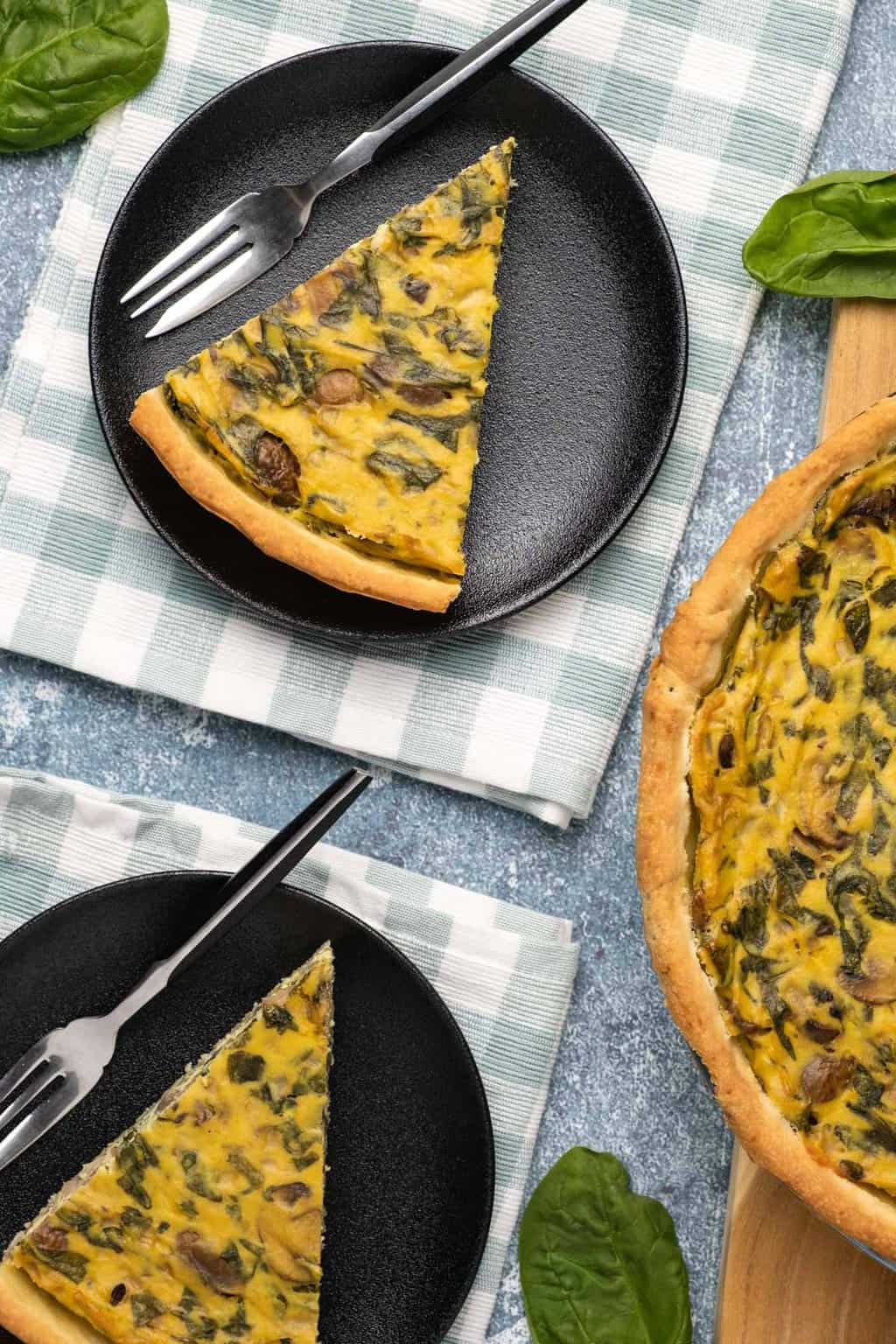 Slices of vegan quiche on black plates with forks. 