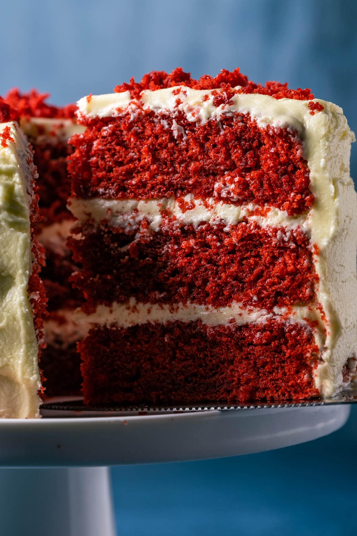 Sliced red velvet cake on a white cake stand.