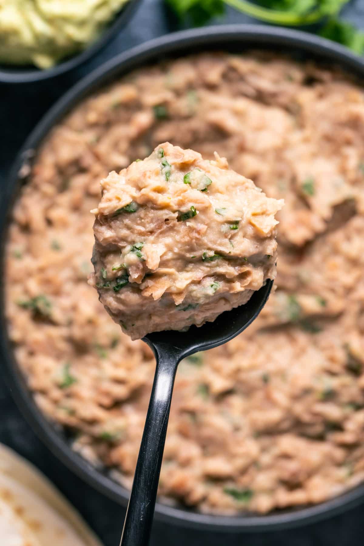 Vegan refried beans in a black bowl with a spoon.
