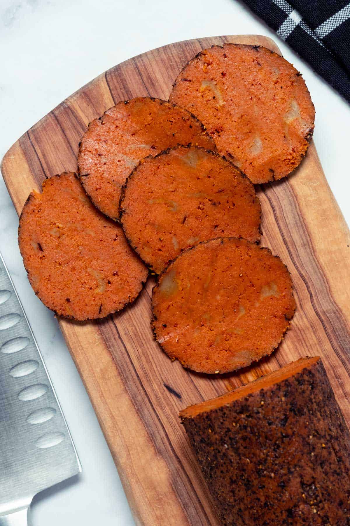 A roll of sliced vegan salami on a wooden board.