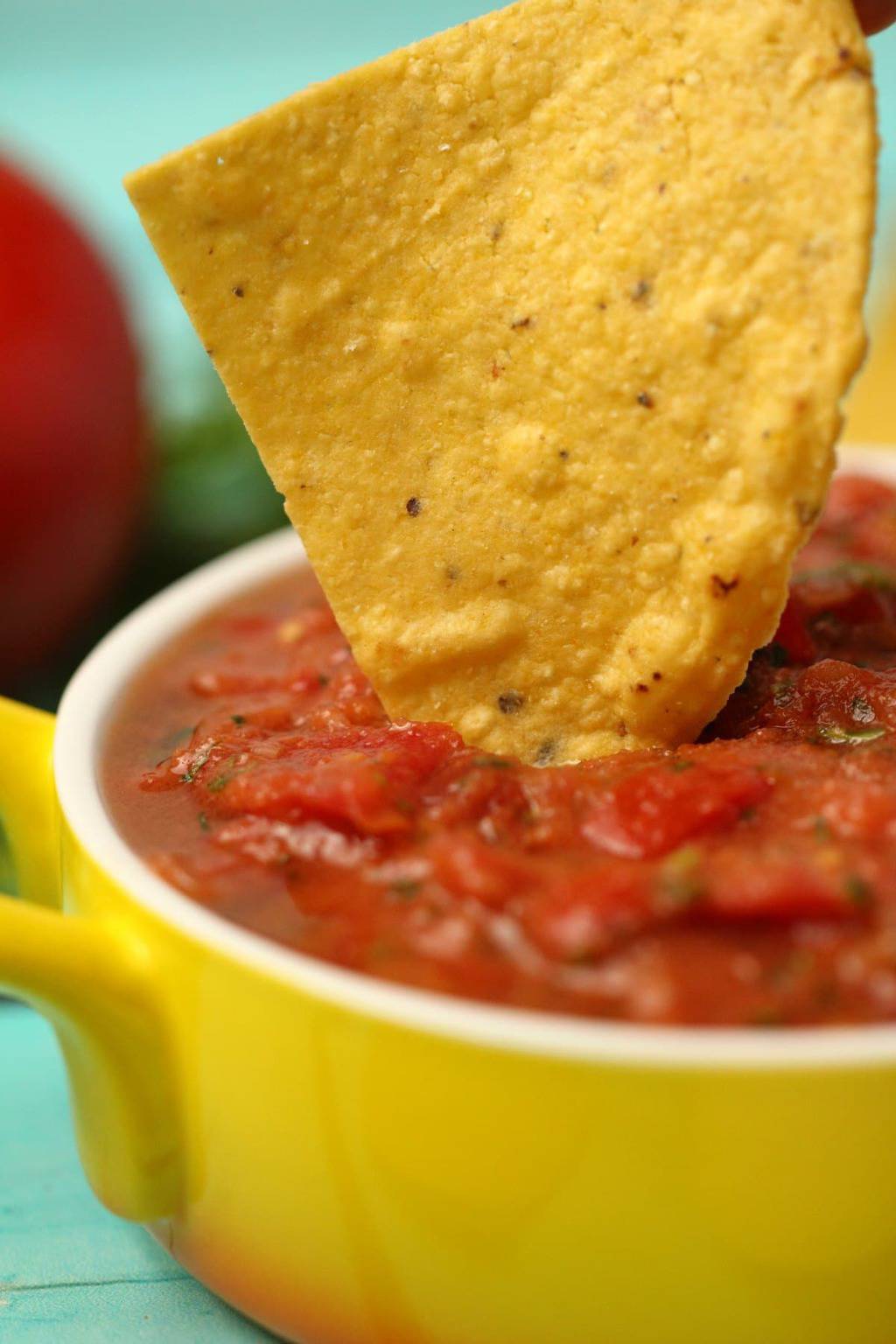 Homemade salsa in a yellow and white glass dish with a tortilla chip dipping in. 