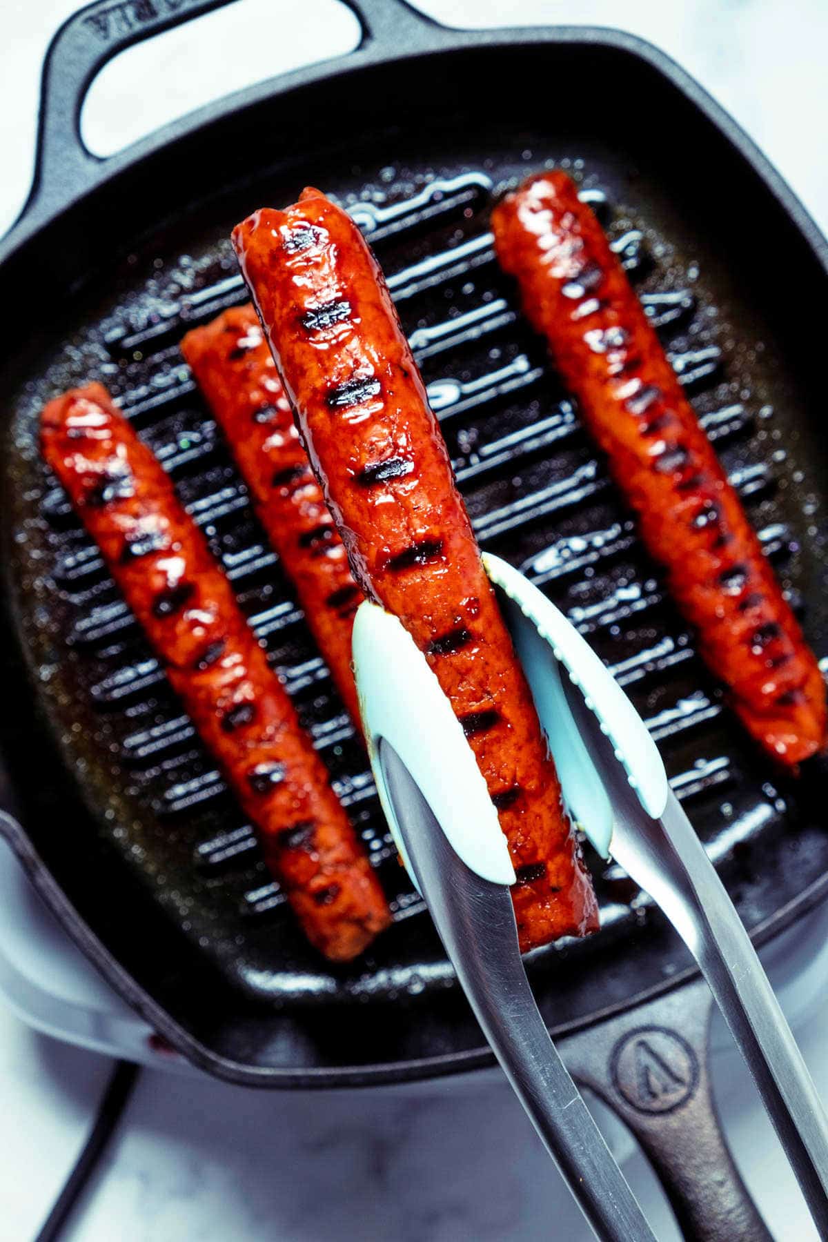Photo of a sausage being lifted out of a grill pan with tongs.