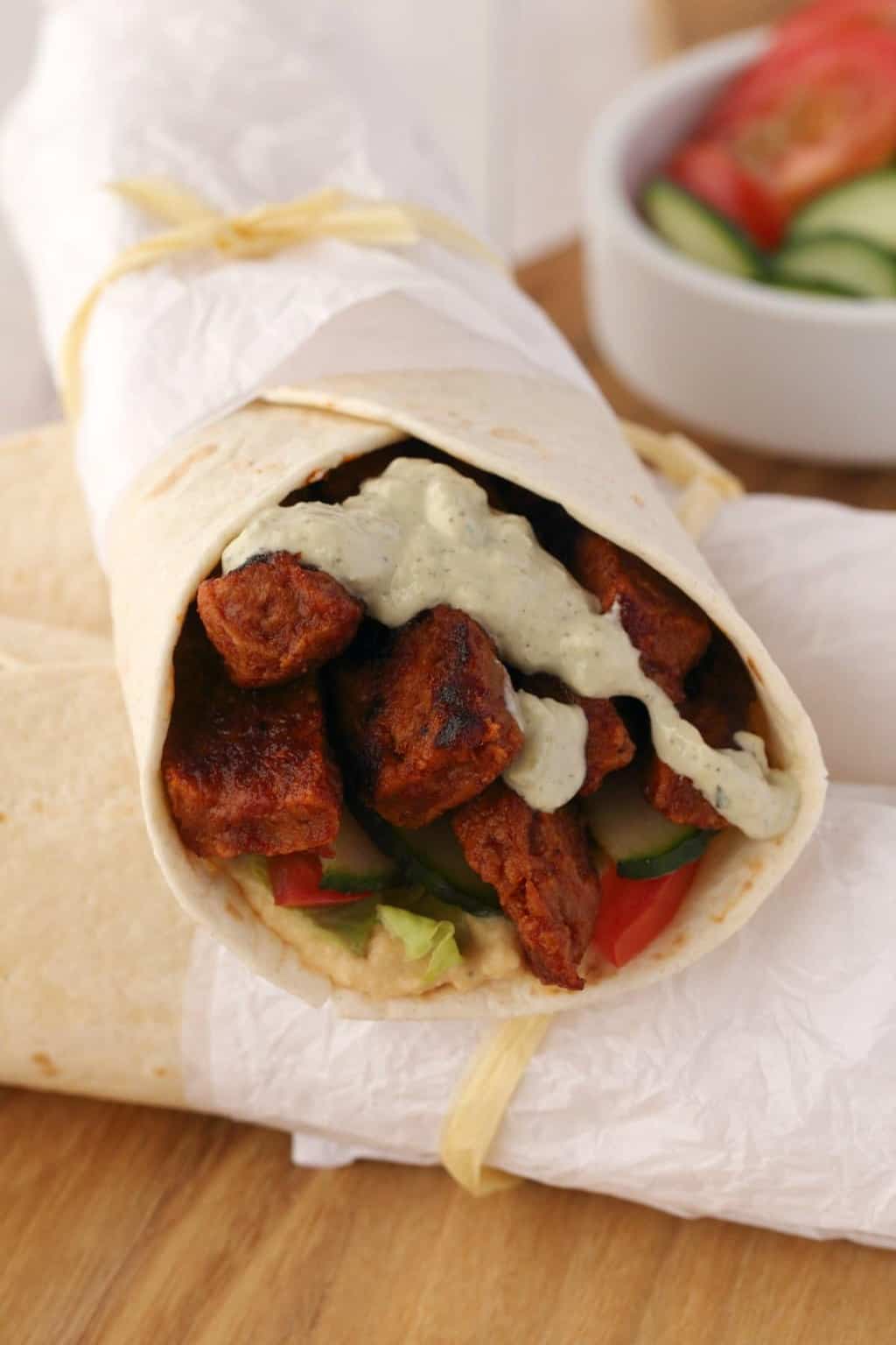Vegan Shawarma stuffed with seitan, veggies and topped with tzatziki, wrapped with white paper and twine. 