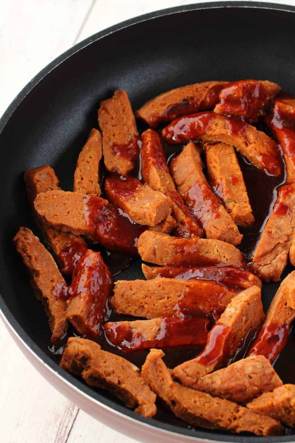 Strips of seitan with marinade sauce poured over them in a frying pan. 