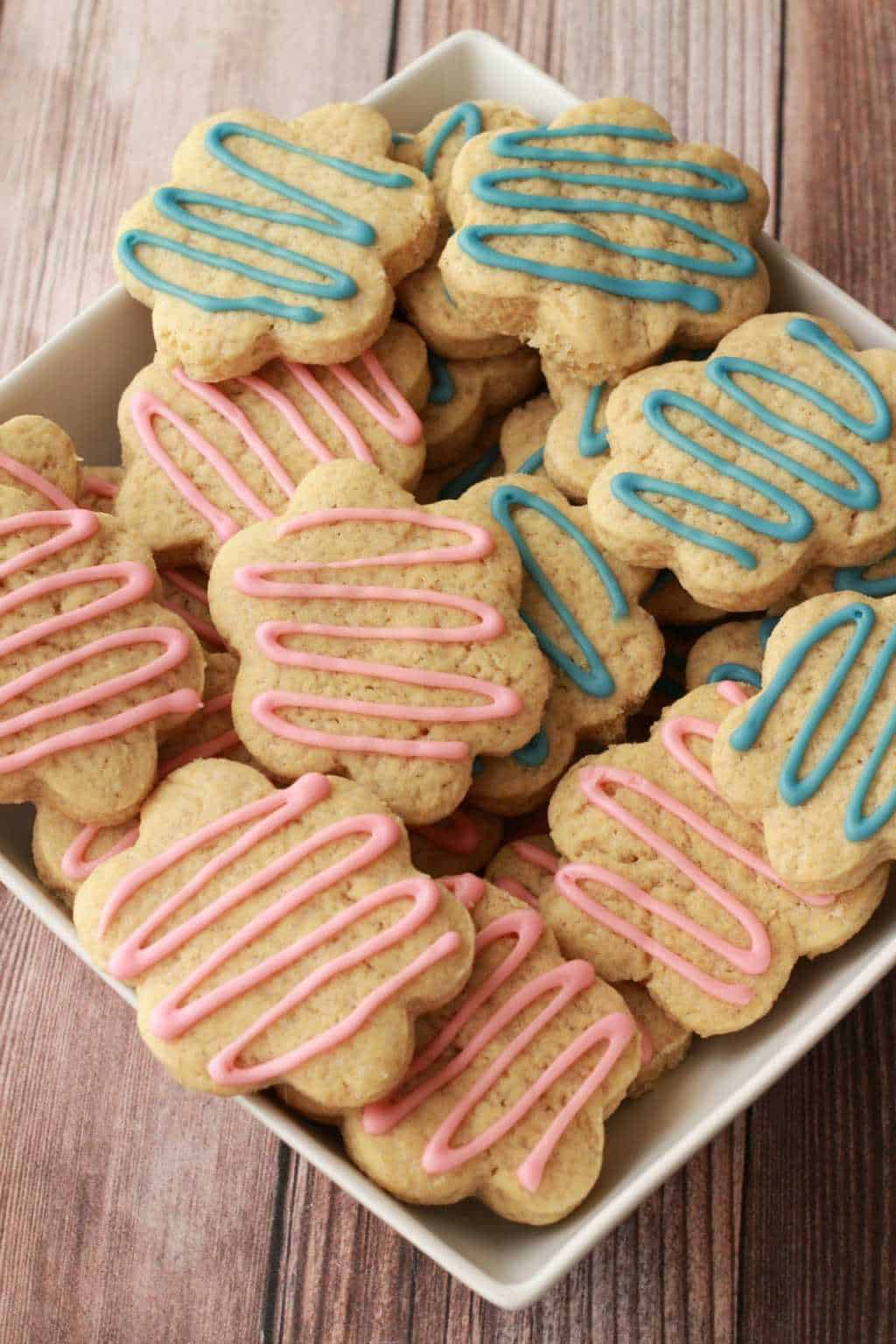 Vegan sugar cookies drizzled with pink and blue frosting in a white bowl. 