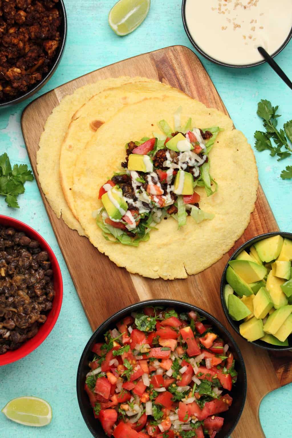 Assembling a vegan taco with lettuce, vegan taco meat, pico de gallo, avocado and tahini sauce. 