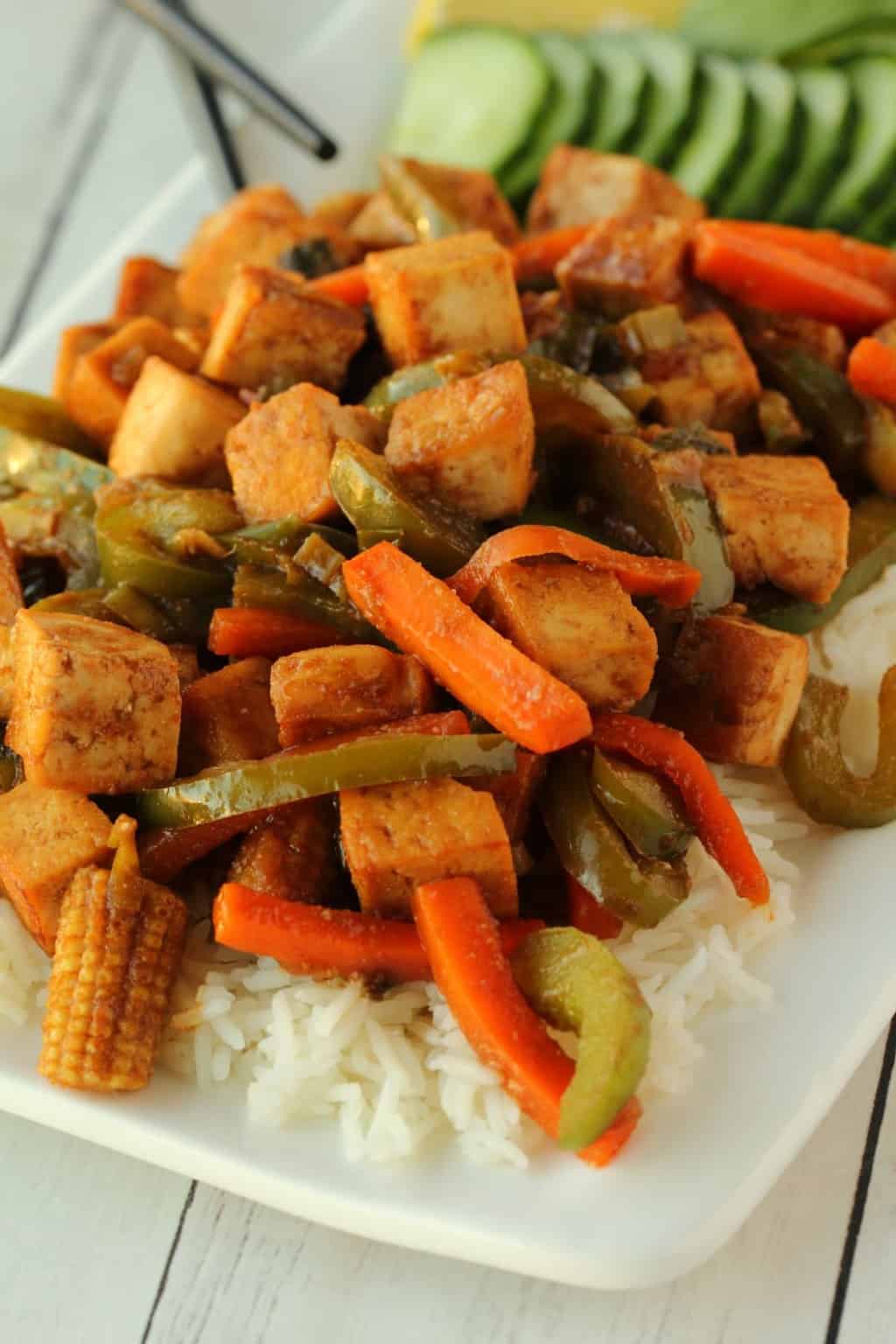 Vegan tofu stir fry served over rice on a white plate with chopsticks. 