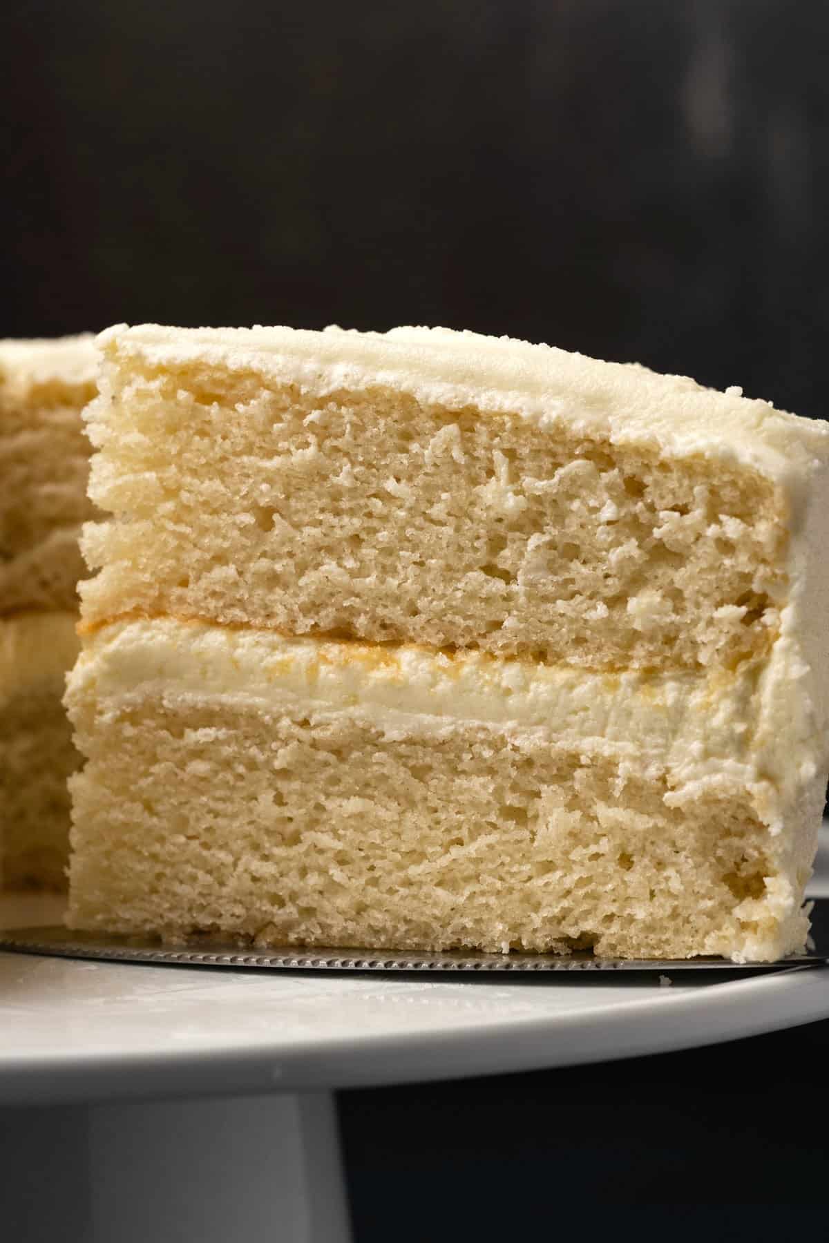 Vegan white cake with a slice cut on a white cake stand. 