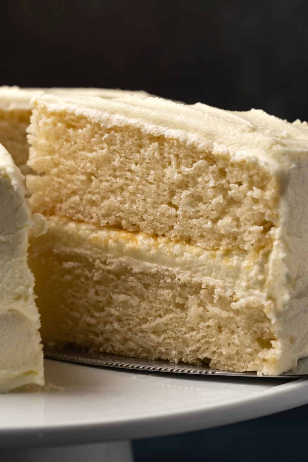 White cake with one slice cut on a white cake stand. 