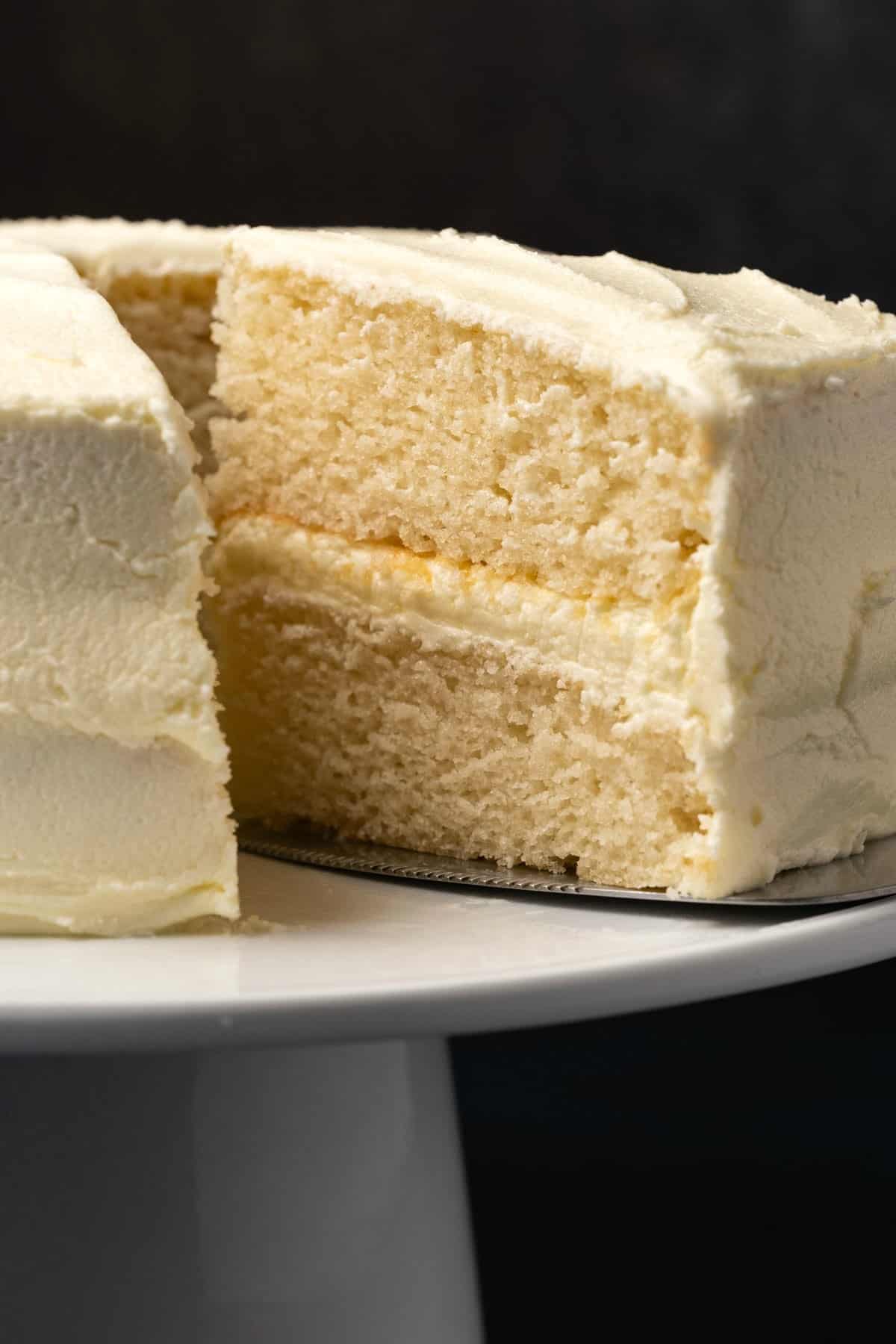 Vegan white cake with one slice cut on a white cake stand. 